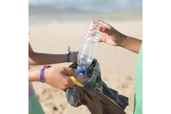 Image People putting empty plastic bottle in bin bag on the beach.